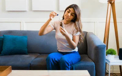 Woman using Magnascent Nascent Iodine supplement dropper on couch at home