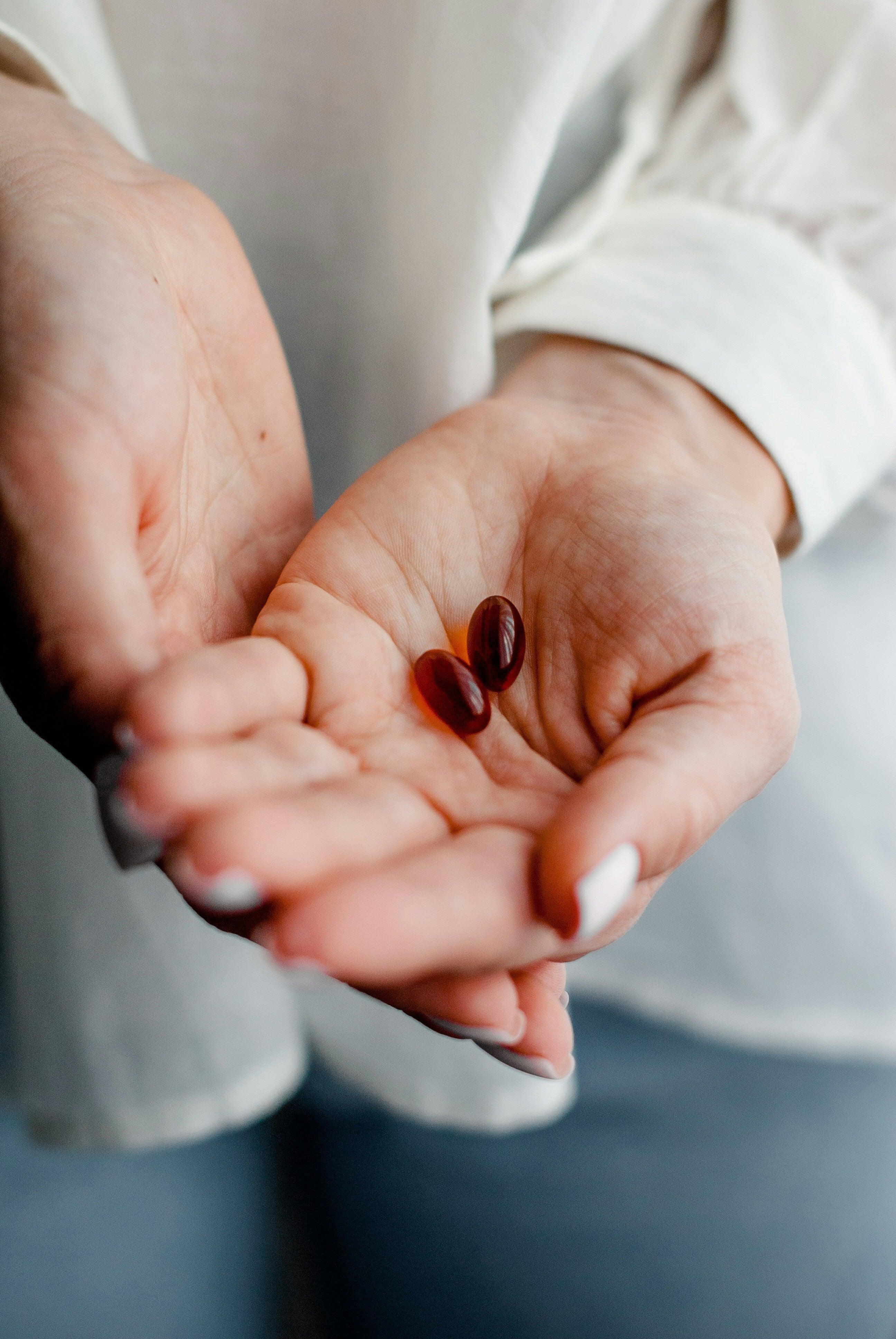 Close-up of hands holding two iodine supplement capsules, Magnascent Iodine focus